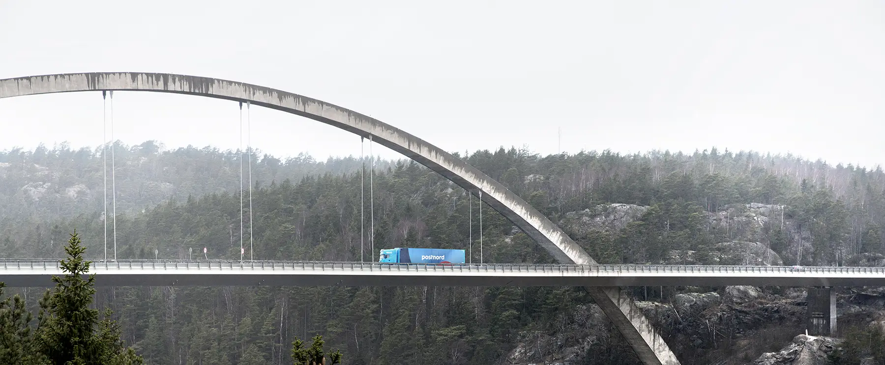 A blue PostNord trck driving along a bridge.